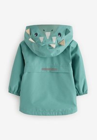Veste de pluie teal avec capuche arborant un design de visage de monstre, incluant des yeux, des dents et des accents beige. Manches élastiques et finition élégante.