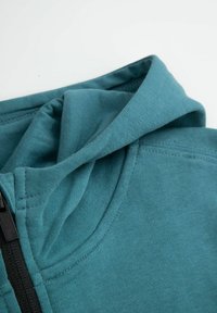 Turkusowy sweatshirt z kapturem o gładkiej fakturze i czarnym zamkiem; posiada złożony kaptur oraz szyte szwy dla zwiększenia trwałości.