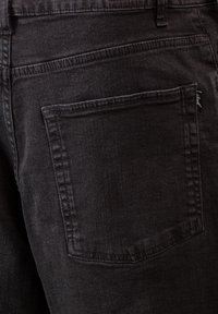 Jeans de mezclilla negra con un único bolsillo trasero, detalles de costura sutiles y una textura suave, destacando un diseño de corte ajustado.