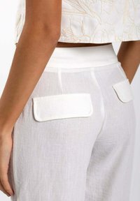 Los pantalones de lino blancos presentan una textura suave y un corte ajustado, con dos bolsillos traseros y una cinturilla sin costuras para un diseño limpio.