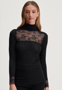 Zwarte coltrui met een bloemenkant yoke en manchetten, met ribbelstructuur en lange mouwen. Het kant heeft een delicaat, ingewikkeld ontwerp.
