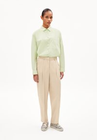 Lichtgroene, langmouwige button-up shirt met een zak; beige, hoge taille broek; schoenen met een zwart-wit zebra patroon.