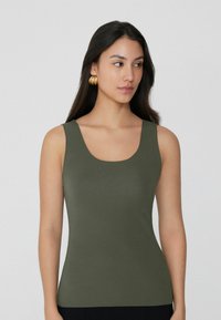 Hladký, bezrukávový top ve tvaru lodičky olivově zelené barvy, s přiléhavým střihem, jemnou texturou a bez viditelných vzorů či akcentů.