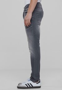 Szürke slim fit farmernadrág kopott textúrával, standard derékpánttal, oldalsó és hátsó zsebbel, fehér sportcipővel párosítva.