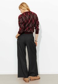 Pull en laine bordeaux avec un motif losange gris et rose, associé à un pantalon large gris foncé et des bottes marron à lacets.