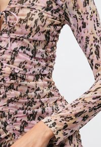 Rufljana obleka z dolgimi rokavi iz lahkega, prosojnega materiala. Ima vzorec živalskega tiska v roza in črni barvi, z teksturiranim nabiranjem ob strani.