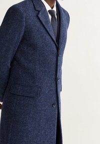 Cappotto in lana testurizzata blu navy, con rever a punta, due bottoni e tasche laterali, vestibilità sartoriale con linee pulite.