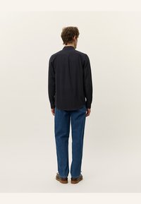 Black long-sleeve shirt with texture detail, button-down collar, and a relaxed fit, paired with blue straight-leg jeans and brown shoes.