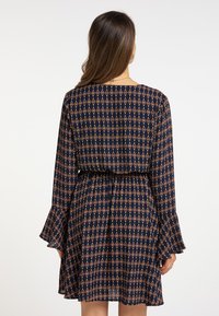 Rochie bleumarin cu un model în diamond în tonuri de auriu și rugină. Mâneci lungi cu un tiv evazat, talie elastică și fustă plisată. Textură de țesătură netedă.