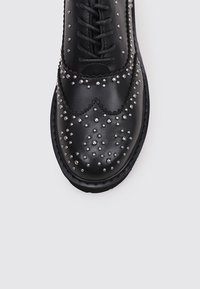 Schwarzer Lederschuh mit perforiertem Design und metallischen Nieten. Verfügt über Schnürsenkel und eine abgerundete Zehenpartie, zeigt eine strukturierte Oberfläche und kontrastierende Nähte.