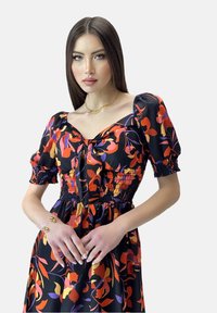 Vestido de estampado floral en negro, con mangas abullonadas, cuerpo fruncido y un detalle de lazo en el escote. Accesorios dorados destacados.