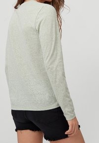 Light green long-sleeve shirt made of soft fabric, featuring a simple round neckline and a relaxed fit, paired with dark denim shorts.