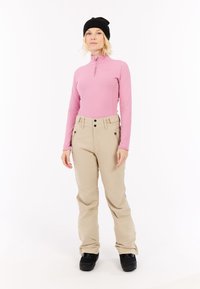 Šviesiai rožinė ilgomis rankovėmis palaidinė su aukštu apykakle, derinama su kreminės spalvos slidinėjimo kelnėmis su kišenėmis ir juodais slidinėjimo batais. Paprastas dizainas, kvėpuojantis medžiaga.