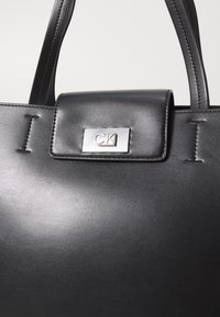 Borsa a spalla in pelle nera con una texture liscia, forma rettangolare e logo CK argentato sulla chiusura a patta. Doppi manici neri.