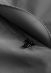 Gray fabric featuring a smooth texture, with a visible zipper and pull in black at the edge, showing stitching along the seam.