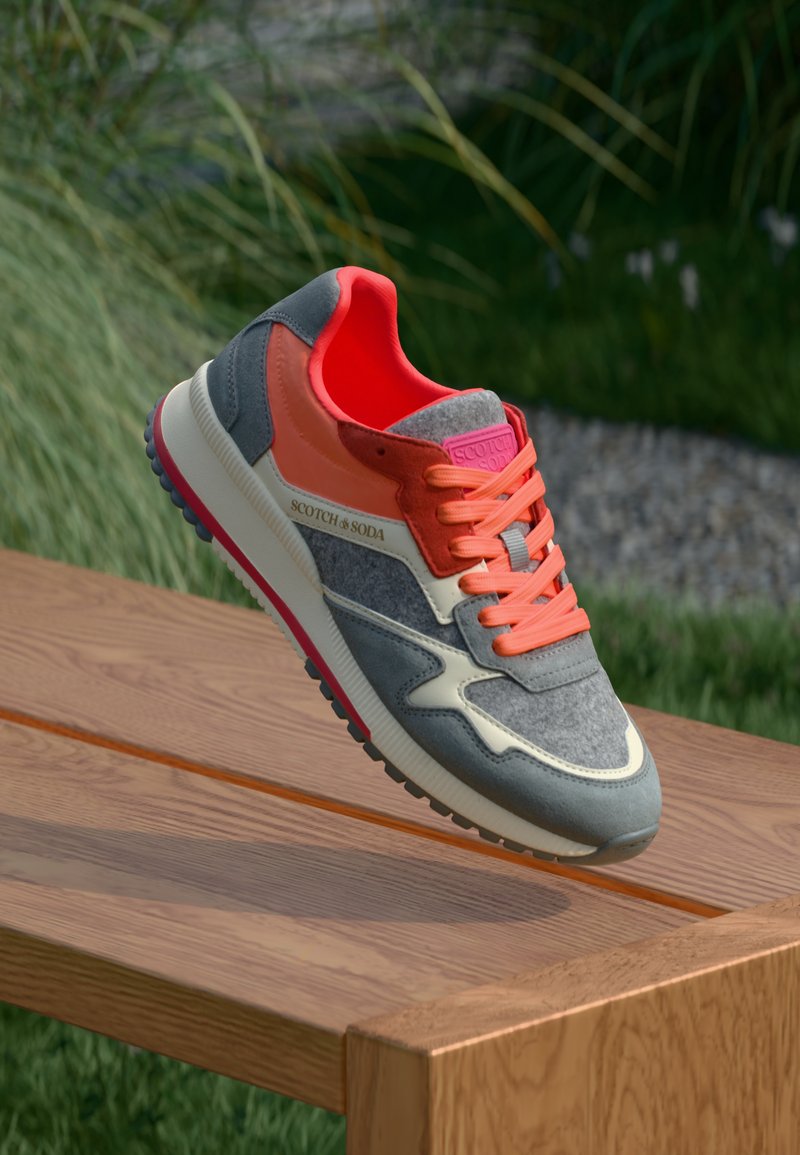 Grå og orange sneakers med en tekstureret overdel, lyserøde detaljer og snørebånd. Har en hvid mellemsål og en sort gummisål.