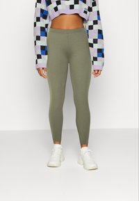 Olive green leggings with a fitted design, made of stretchy material. Worn with a cropped, multi-colored checkered sweater and white sneakers.