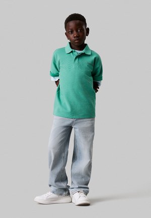 Grøn polo-shirt med stribet tekstur, korte ærmer og krave, parret med lyseblå jeans og hvide sneakers.