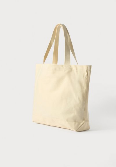 Bolsa de tela en amarillo pálido con dos asas de tela resistentes. Presenta una forma rectangular y una textura sutil, adecuada para el uso diario.