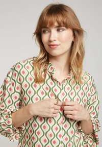 Chemise à boutons avec un motif géométrique vert, rose et blanc. Tissu léger, manches longues et coupe décontractée avec poignets roulés.