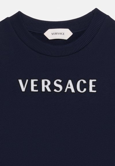 Pull bleu marine avec col rond côtelé et logo Versace blanc brodé sur la poitrine, sous l’étiquette à l’intérieur du col.