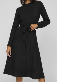 Black, knitted dress with a ribbed texture, long sleeves, a crew neckline, and a fabric belt tied at the waist. A-line silhouette.