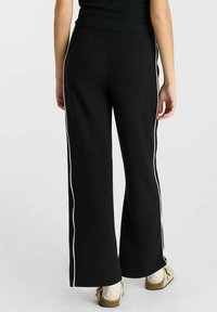 Zwarte wijde broek van zacht materiaal met witte zijkanten. Heeft een gladde textuur en een ontspannen pasvorm, die eindigt bij de enkel.