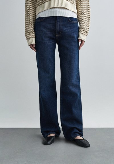 Wide-leg dark blue denim jeans with a smooth texture and classic five-pocket design, paired with black flat shoes and a knitted sweater.