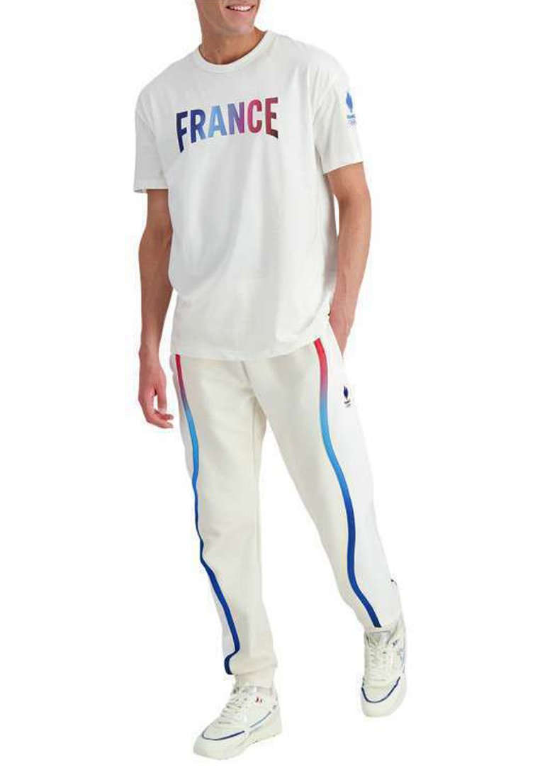 T-shirt blanc avec "FRANCE" en lettres multicolores, associé à un pantalon blanc avec des bandes latérales bleues et rouges et des baskets blanches.