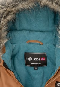 Kinderjas in bruin met een teal fleece voering en nep bont trim op de capuchon, met het Trollkids merklabel en maat 104 label zichtbaar.