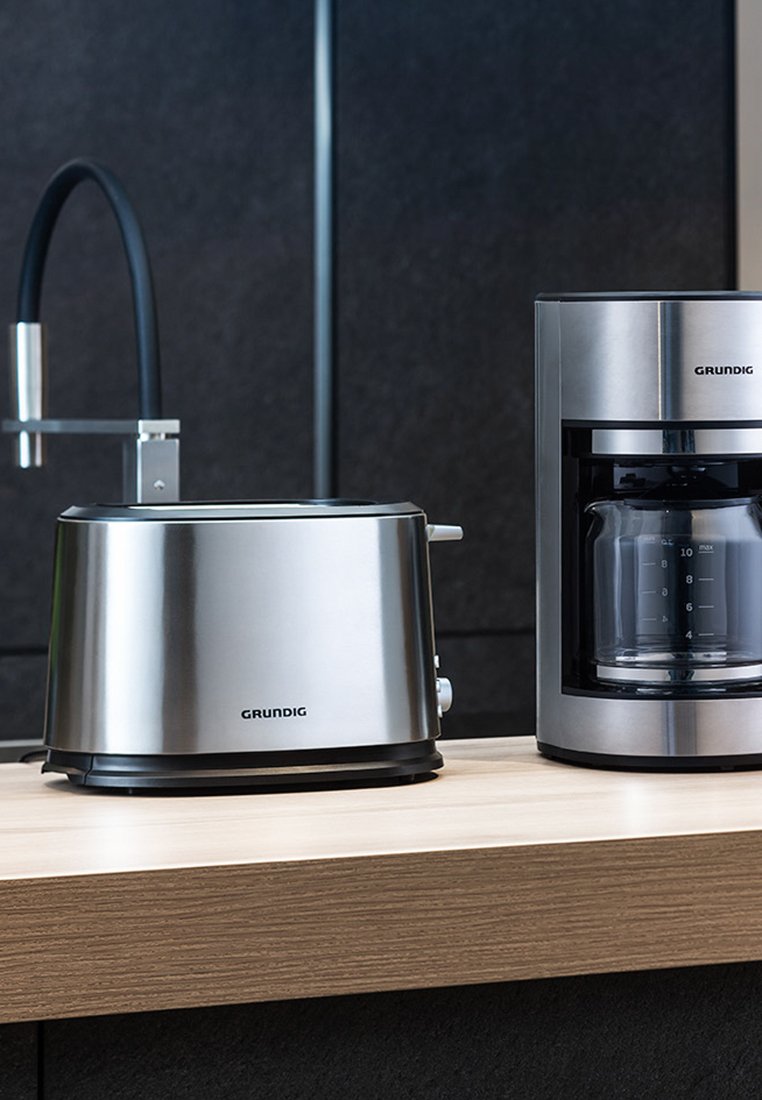 Edelstahl-Toaster und Kaffeemaschine auf einer Holzküchenplatte; beide haben ein elegantes Design mit schwarzen Akzenten und klaren Maßangaben.