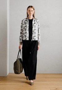 Giacca bianca e grigia a fantasia con maniche lunghe, top nero, pantaloni neri a gamba larga e una grande borsa a tracolla grigia. Scarpe in toni della terra.