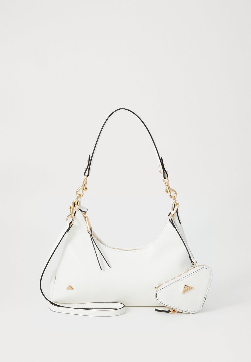 Sac à main blanc avec garniture noire, ferrures dorées, fermeture éclair et petite pochette triangulaire attachée sur fond uni.