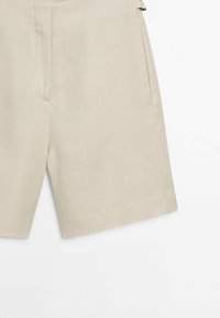Shorts beige longueur genou avec poches latérales et braguette zippée, fabriqués dans un tissu texturé.