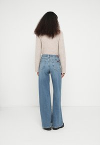 Jeans de ganga azul claro com corte largo, cintura alta e acabamento esbatido. Apresentam dois bolsos nas costas e um emblema de couro com o logotipo na cintura.