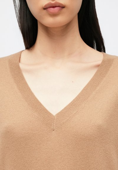V-kaelusega kampsun helepruuni toonis, valmistatud pehmest kangast, millel on sooniline kaelus. Sile tekstuur ja minimalistlik disain.