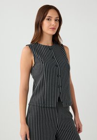 Top senza maniche a righe bianche e nere con scollatura rotonda e chiusura a bottoni, caratterizzato da una vestibilità sartoriale e una texture liscia.