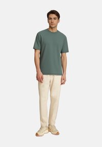 Teal zöld, rövidujjú póló, texturált anyagból, világos bézs nadrággal és krém színű sportcipőkkel párosítva.