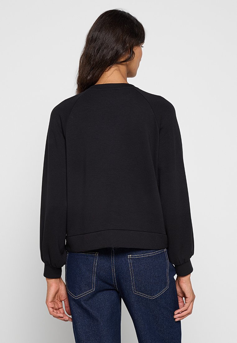 Zwarte sweatshirt met een raglan mouwontwerp, voorzien van een geribde kraag en boorden, en een ruime pasvorm, gecombineerd met donkere spijkerbroek.