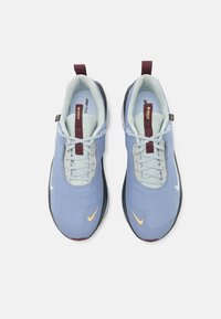 Scarpe da atletica azzurro chiaro con un design elegante, dettagli grigi, tomaia texturizzata, lacci bordeaux e suole in gomma nera. Logo Nike swoosh ben visibile.