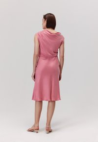 Różowa, bezrękawnikowa sukienka z drapowaną tylną częścią. Gładka tekstura, do kolan, o luźnym kroju. W połączeniu z lekkimi, sandałami na cienkich paskach.