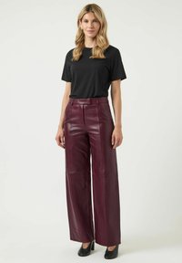 Zwarte T-shirt met korte mouwen gecombineerd met hoog getailleerde, wijdvallende bordeauxlederen broek. De broek heeft een gladde textuur en naaddetails.