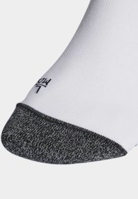 Chaussette de sport blanche avec un embout texturé noir et un détail de logo. Le tissu semble lisse et extensible.