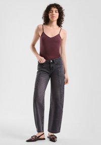 Bordeaux mouwloze body gecombineerd met hooggesneden, wijde, donkergrijze spijkerbroek en donkere platte schoenen met decoratieve hardware.