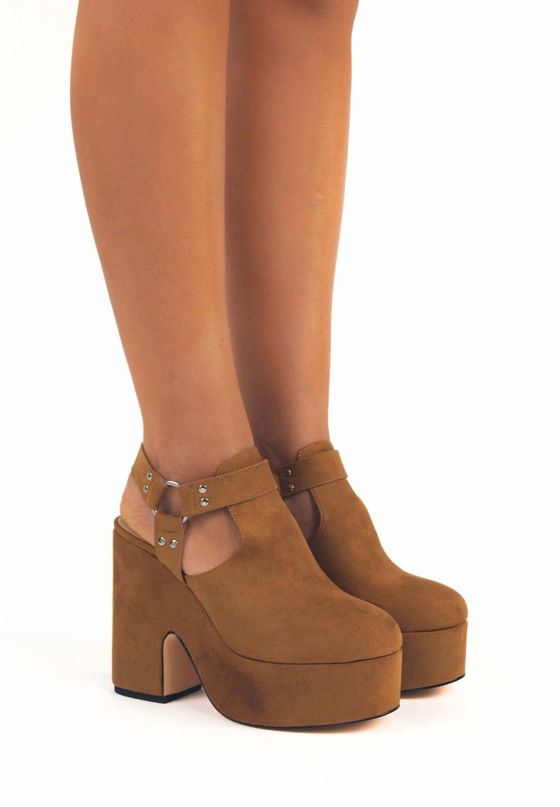 Tacchi a piattaforma in suede marroni, con un design a taglio, cinturino alla caviglia e accenti in metallo argentato. Tacco spesso e punta arrotondata.