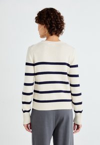 Sweter w paski w odcieniach kremowym i granatowym, dzianinowa tekstura, ściągacze na mankietach i u dołu, okrągły dekolt, lekki z dopasowanym krojem.