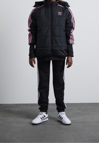 Black puffer jacket with pink stripes, paired with black joggers featuring white side stripes. White sneakers with black accents complete the look.