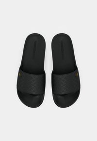 Une paire de sandales à glisser noires avec un motif logo texturé sur toute la surface et un petit emblème de marque en ton doré sur les lanières.