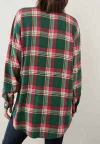 Chemise en flanelle à carreaux verts, rouges et gris, manches longues et ourlet arrondi, présentant de grands motifs à carreaux et des poignets à boutons.