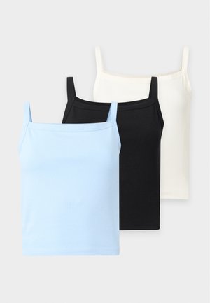 Vrouw die een zwarte mouwloze top en lichtblauwe jeans met wijde pijpen draagt, en een kleine groene handtas in één hand houdt.